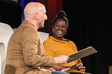 Speaker and host laughing during a fireside chat at UXDX